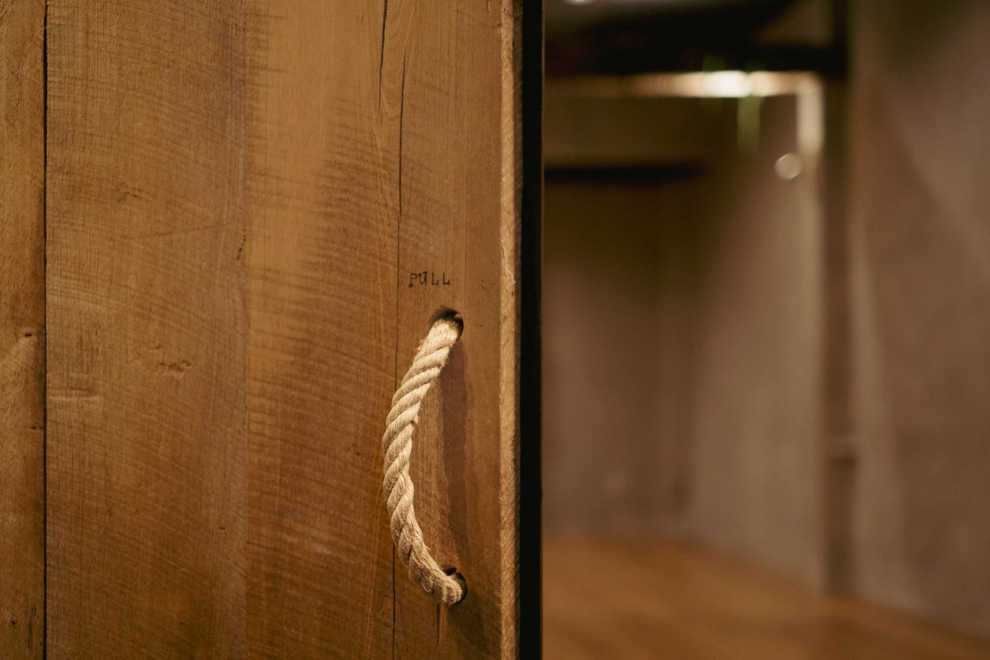 A rope handle on a reclaimed wooden studio door, with warm limewashed walls beyond.