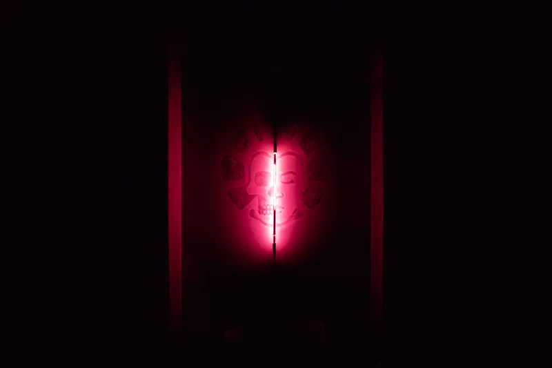 The REWILD skull artwork in darkness beside a vertical pink-red neon light.